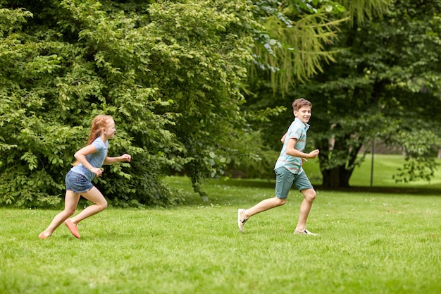 concept d'amitié, d'enfance, de loisirs et de personnes - groupe d'enfants ou d'amis heureux jouant à un jeu de rattrapage et courant dans un parc d'été