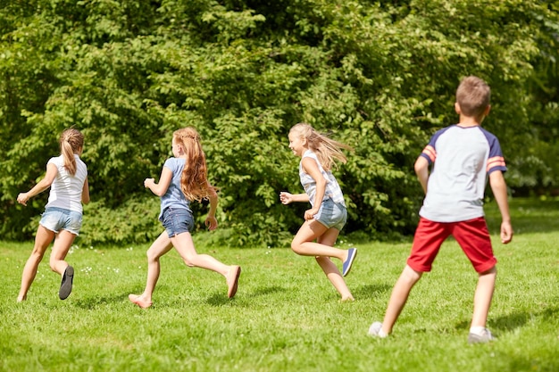 concept d'amitié, d'enfance, de loisirs et de personnes - groupe d'enfants ou d'amis heureux jouant à un jeu de rattrapage et courant dans un parc d'été