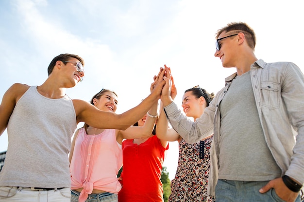 Concept d'amitié, de loisirs, d'été, de gestes et de personnes - groupe d'amis souriants faisant cinq hautes à l'extérieur