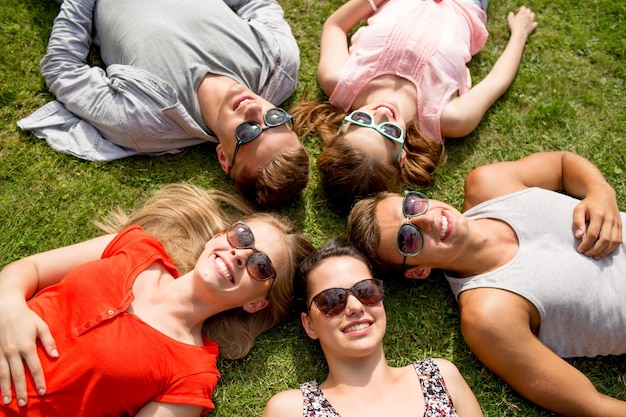 concept d'amitié, de loisirs, d'été et de personnes - groupe d'amis souriants allongés sur l'herbe en cercle à l'extérieur