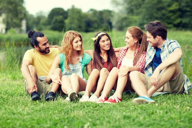 concept d'amitié, de loisirs, d'été et de personnes - groupe d'amis souriants assis sur l'herbe et parlant à l'extérieur