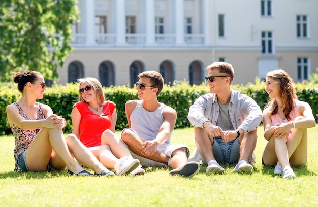 concept d'amitié, de loisirs, d'été et de personnes - groupe d'amis souriants à l'extérieur assis sur l'herbe dans le parc