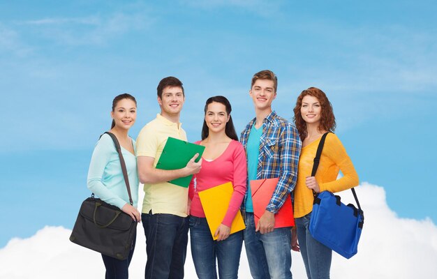 Concept d'amitié, de rêve, d'éducation et de personnes - groupe d'adolescents souriants avec des dossiers et des sacs d'école sur un ciel bleu avec un fond de nuage blanc