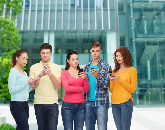 concept d'amitié, de technologie, d'éducation, d'affaires et de personnes - groupe d'adolescents sérieux avec des smartphones sur fond de campus