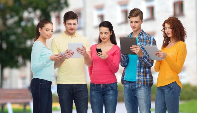 concept d'amitié, de technologie, d'éducation, d'école et de personnes - groupe d'adolescents souriants avec smartphones et ordinateurs tablettes sur fond de campus