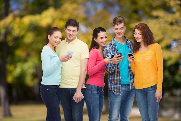 concept d'amitié, de technologie, de nature et de personnes - groupe d'adolescents souriants avec des smartphones sur fond de parc