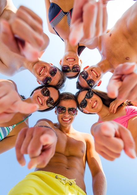 Concept d'amitié, de vacances d'été, de gestes et de personnes - groupe d'amis souriants portant des maillots de bain et pointant le doigt sur vous debout en cercle sur le ciel bleu