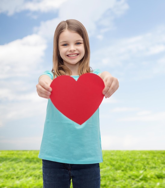 concept d'amour, de bonheur et de personnes - petite fille souriante donnant un coeur rouge