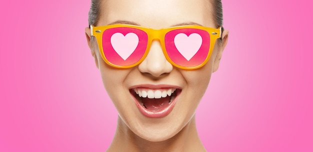 concept d'amour, de bonheur et de saint valentin - adolescente étonnée en lunettes de soleil avec des coeurs sur fond rose