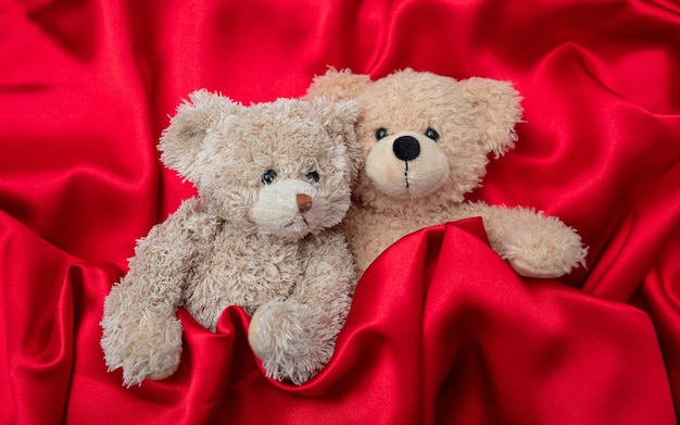 Concept d'amour câlin serré deux ours en peluche embrassant comme un couple au lit fond de satin rouge