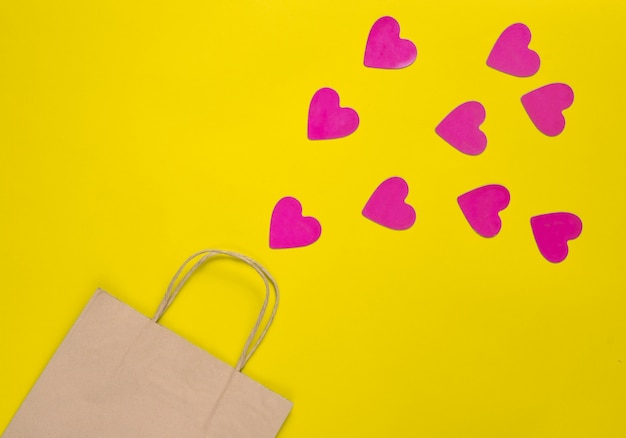 Le concept de l'amour du shopping. Un sac en papier pour faire du shopping et beaucoup de coeurs décoratifs sur fond jaune. La Saint-Valentin. Vue de dessus.