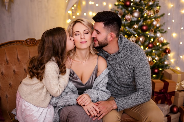 concept d'amour et de famille père et fille embrassant leur heureuse maman près de l'arbre de Noël