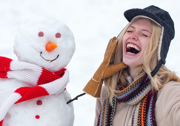 Concept d'amour d'hiver. Happy girl plaing avec un bonhomme de neige sur une promenade d'hiver enneigée. Faire bonhomme de neige et