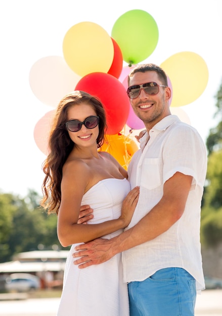 concept d'amour, de mariage, d'été, de rencontres et de personnes - couple souriant portant des lunettes de soleil avec des ballons étreignant dans le parc