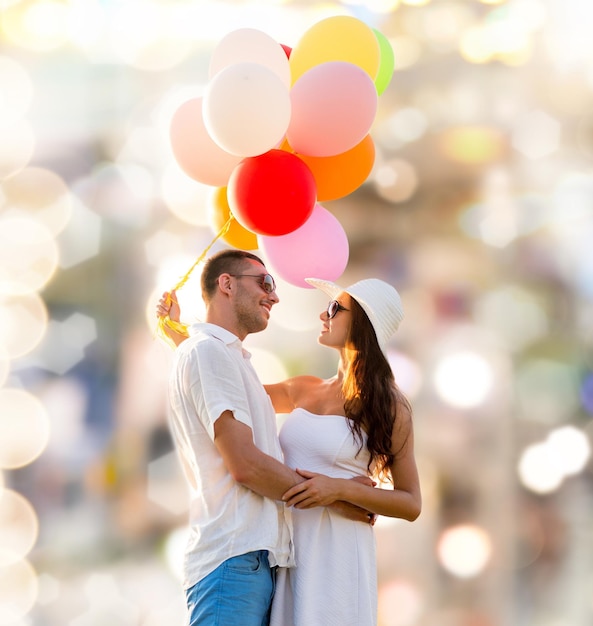 concept d'amour, de mariage, d'été, de rencontres et de personnes - couple souriant portant des lunettes de soleil avec des ballons étreignant sur fond de lumières