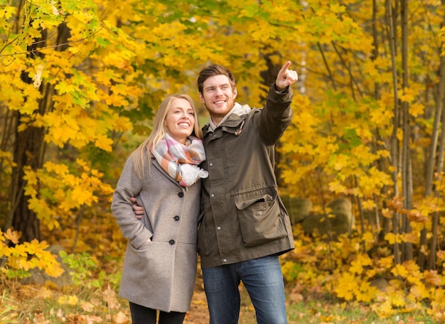 concept d'amour, de relation, de famille et de personnes - couple souriant étreignant et pointant le doigt dans le parc d'automne