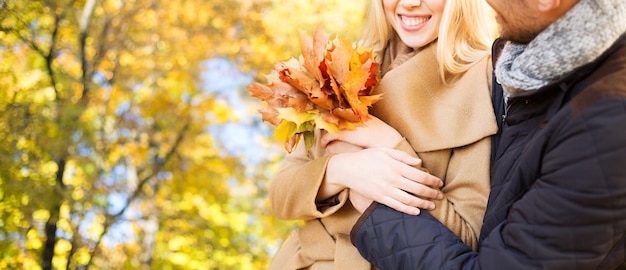 concept d'amour, de relation, de famille, de saison et de personnes - gros plan d'un couple souriant avec un tas de feuilles étreignant sur fond naturel d'automne