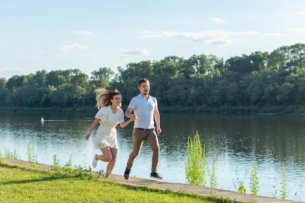 Concept d'amour et de relation - L'homme et la femme heureux qui court dans un parc près d'un lac