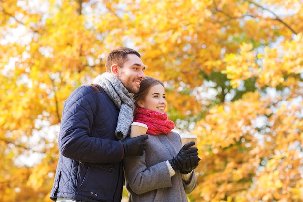 concept d'amour, de relation, de saison, d'amitié et de personnes - couple souriant avec des tasses à café dans le parc d'automne