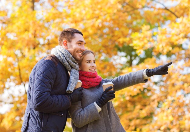 concept d'amour, de relation, de saison, d'amitié et de personnes - couple souriant avec des tasses à café dans le parc d'automne