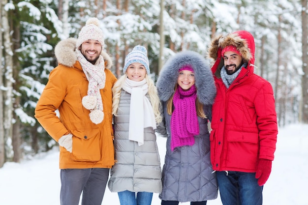 concept d'amour, de relation, de saison, d'amitié et de personnes - groupe d'hommes et de femmes souriants marchant dans la forêt d'hiver