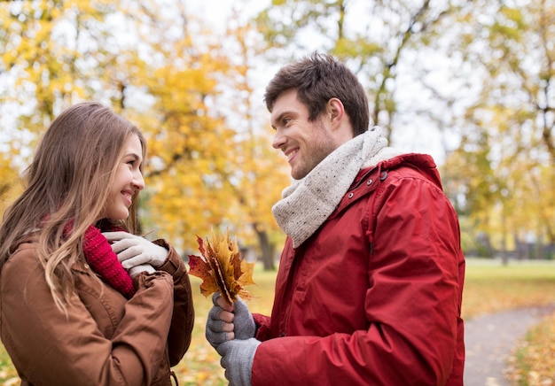 concept d'amour, de relations, de saison et de personnes - jeune couple heureux avec des feuilles d'érable dans le parc d'automne