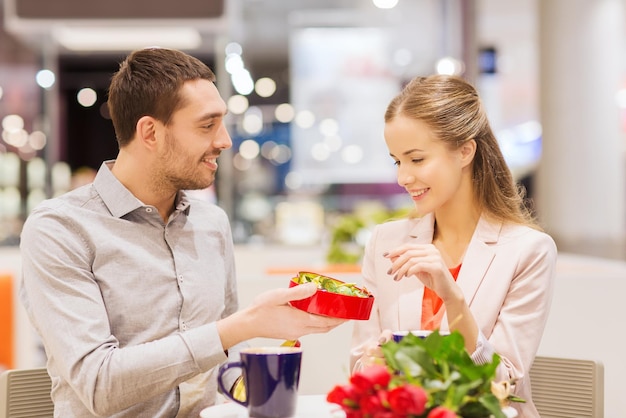 concept d'amour, de romance, de saint valentin, de couple et de personnes - jeune couple heureux avec des fleurs rouges et une boîte-cadeau ouverte au café mall