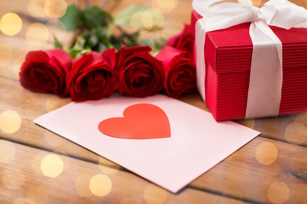 concept d'amour, de romance, de saint valentin et de vacances - gros plan d'une boîte cadeau, de roses rouges et d'une carte de voeux avec coeur sur bois