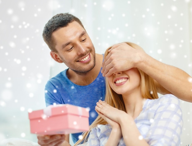 concept d'amour, de vacances, de fête et de famille - un homme souriant surprend sa petite amie avec un cadeau à la maison