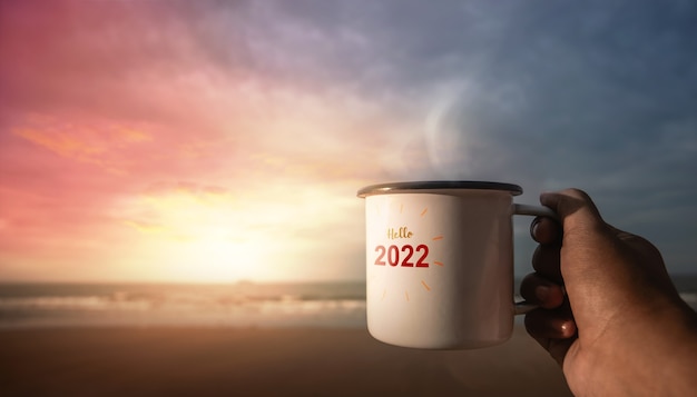 Concept de l'année 2022. Commencez et célébrez une nouvelle année en buvant du café chaud sur la plage au lever du soleil. Dites bonjour à l'année 2022. Vue PDV