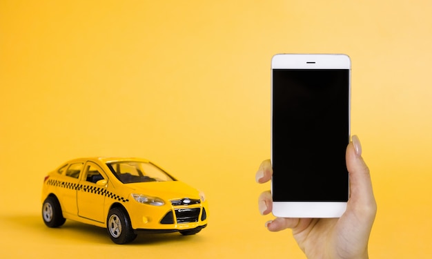 Concept d'application en ligne de taxi urbain mobile. Modèle de voiture de taxi jaune jouet. Main tenant le téléphone intelligent avec l'application de service de taxi sur l'écran.
