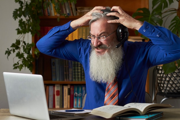 Concept d'apprentissage à distance. Professeur frénétique tuteur regardant un ordinateur portable et tenant sa tête, mise au point sélective
