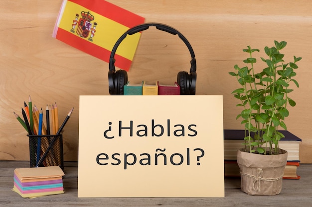 Concept d'apprentissage de la langue espagnole papier avec texte hablas espanol hablas espanol drapeau de l'Espagne livres écouteurs crayons sur fond de bois