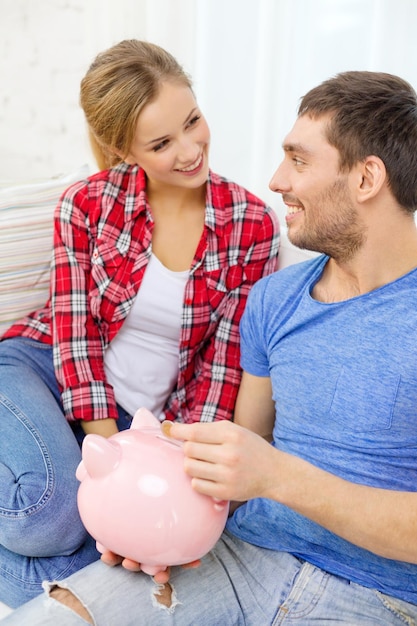 concept d'argent, de maison, de finances et de relations - couple souriant avec tirelire assis sur un canapé