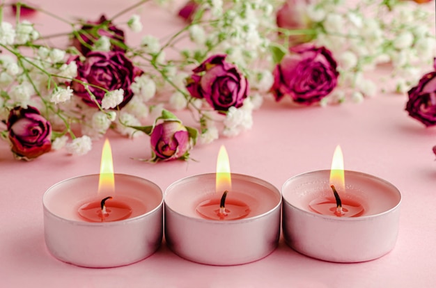 Concept d'aromathérapie. Trois bougies allumées et roses sèches sur rose.