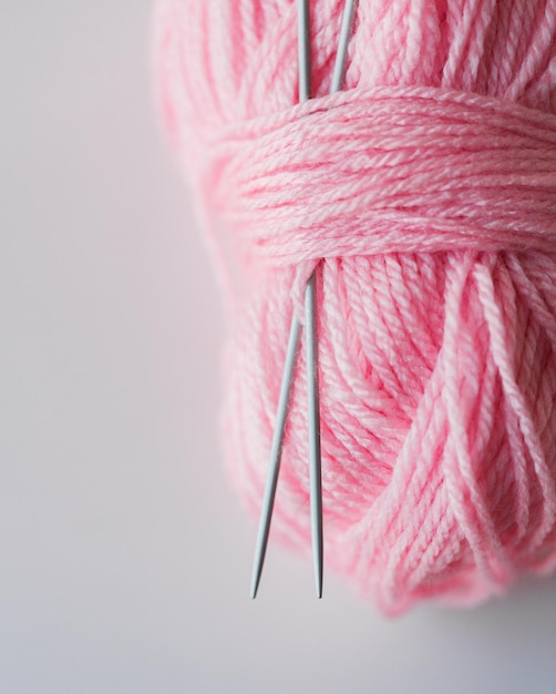 concept d'artisanat et de couture - gros plan d'aiguilles de tricot et de boule de fil rose sur blanc