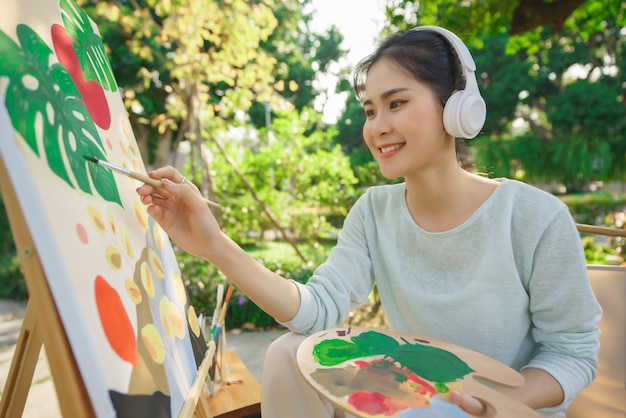 Concept d'artiste Une artiste féminine porte un casque pour écouter de la musique et peindre une image sur toile