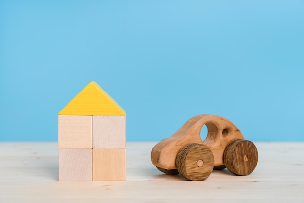 Photo le concept d'assurance automobile et immobilière voiture jouet en bois et maison faite de blocs de bois jouet sur fond bleu