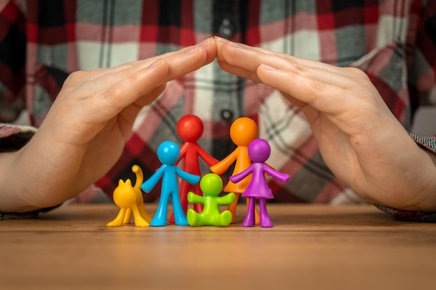 Concept d'assurance familiale avec des figurines familiales colorées couvertes par les mains sur une table en bois Photo de sécurité et de soutien