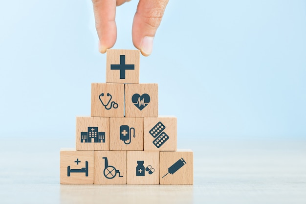 Concept d'assurance maladie, main organisant l'empilement de blocs de bois avec l'icône de soins de santé médical.