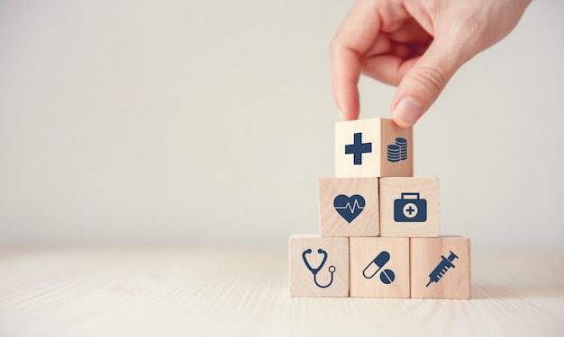 Photo concept d'assurance maladie, réduire les frais médicaux, cube en bois flip hand avec icône santé médical et pièce de monnaie sur fond de bois, espace de la copie.
