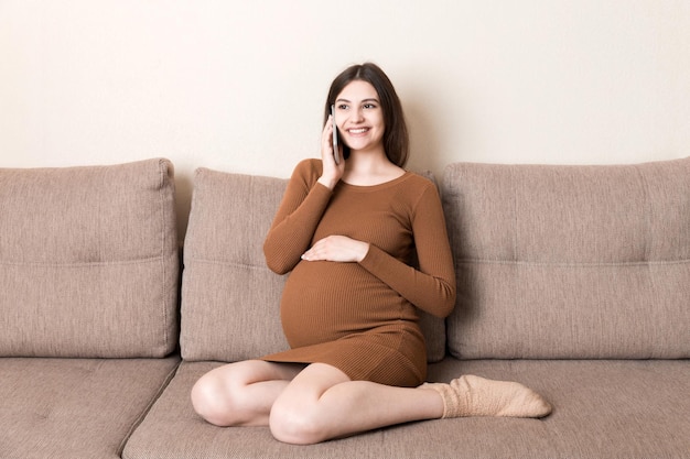 Concept d'attente de grossesse heureuse femme enceinte parlant sur smartphone à la maison