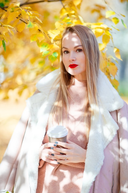 Concept de l'automne - belle femme buvant du café dans un parc en automne sous le feuillage d'automne