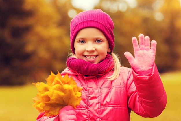concept d'automne, d'enfance, de bonheur et de personnes - belle petite fille heureuse avec un bouquet de feuilles d'érable agitant la main à l'extérieur