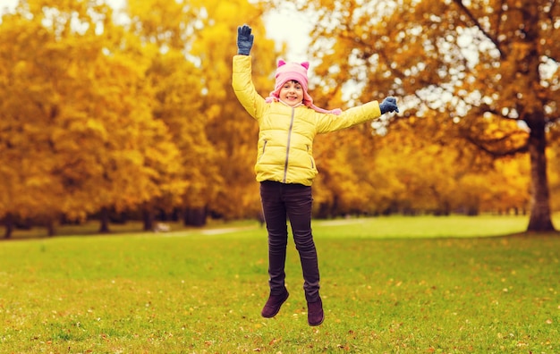 concept d'automne, d'enfance, de bonheur et de personnes - petite fille heureuse avec les mains levées sautant et s'amusant à l'extérieur