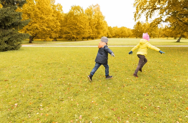 concept d'automne, d'enfance, de loisirs et de personnes - groupe de petits enfants heureux jouant au jeu de balises et courant dans le parc à l'extérieur