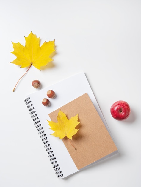 Concept d'automne à plat avec des feuilles d'érable jaunes sur un cahier et un bloc-notes et une pomme rouge sur un tableau blanc Vue de dessus et espace de copie