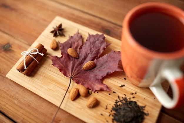 concept d'automne et de saison - tasse de thé, feuille d'érable et amande sur planche de bois