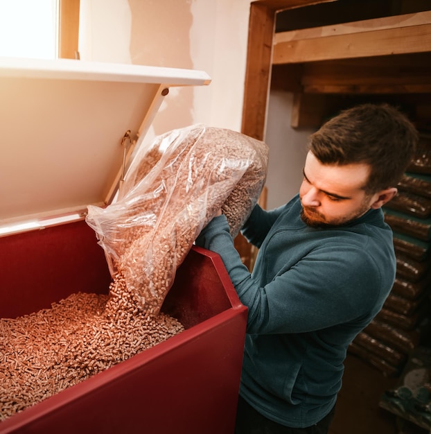 Concept d'avenir durable L'homme charge des granulés de bois dans un poêle de chauffage avec sac Chauffage domestique en hiver