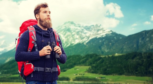 concept d'aventure, de voyage, de tourisme, de randonnée et de personnes - homme avec sac à dos rouge et jumelles sur fond de montagnes alpines